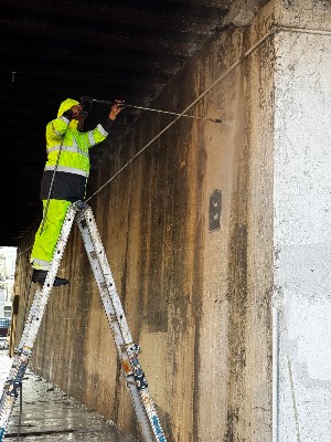 Crew member on a ladder pressure washing a concrete wall