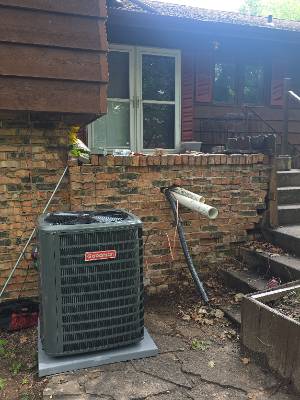 Goodman air conditioner condenser set on a pad beside a brick patio