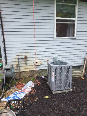 Air conditioner condenser being serviced alongside a home