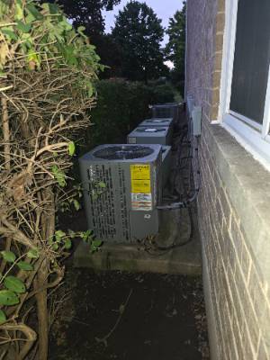 Two air conditioner condensers installed along a brick wall at dusk