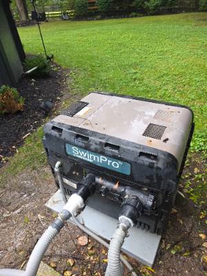 SwimPro pool heat pump installed on a pad next to a backyard