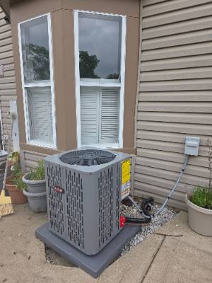 New air conditioner condenser set on a pad beside a bay window