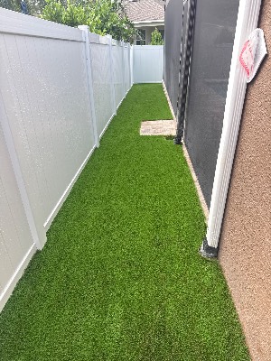 Artificial grass fitted down a narrow side yard between a fence and a pool screen