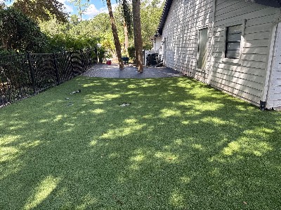 Newly laid artificial grass along the side of a home, with weed barrier ready for the next section