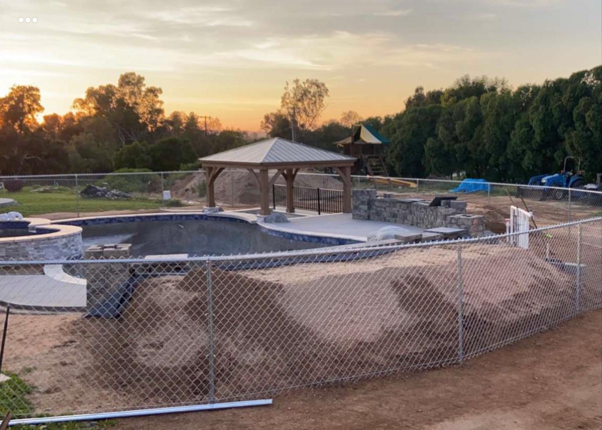 New chain link fence enclosing a backyard pool build at sunset