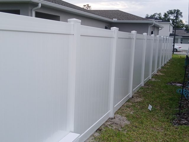 A white vinyl privacy fence running the side of an Orlando house over mown grass