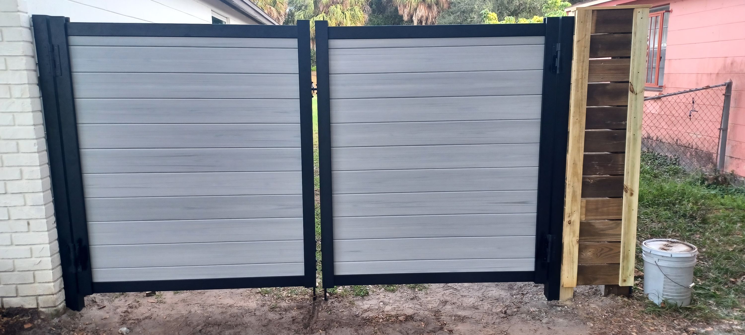 A double drive gate in grey composite board on a black steel frame, hung square between its posts