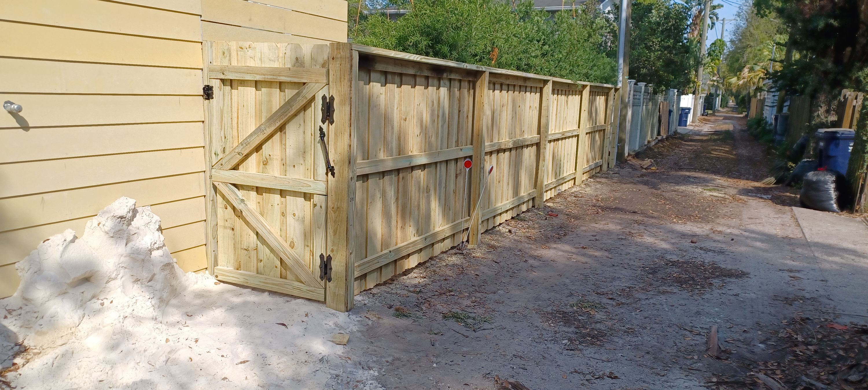 A wood gate braced diagonally and hung on heavy hinges, with the ground still open at its post footing