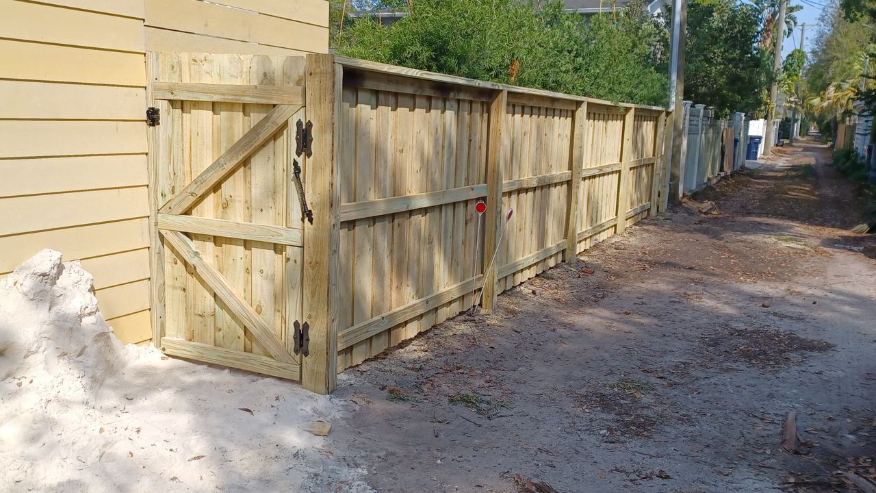A wood gate braced diagonally and hung on heavy hinges, with the ground still open at its post footing