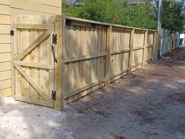 A wood gate braced diagonally and hung on heavy hinges, with the ground still open at its post footing