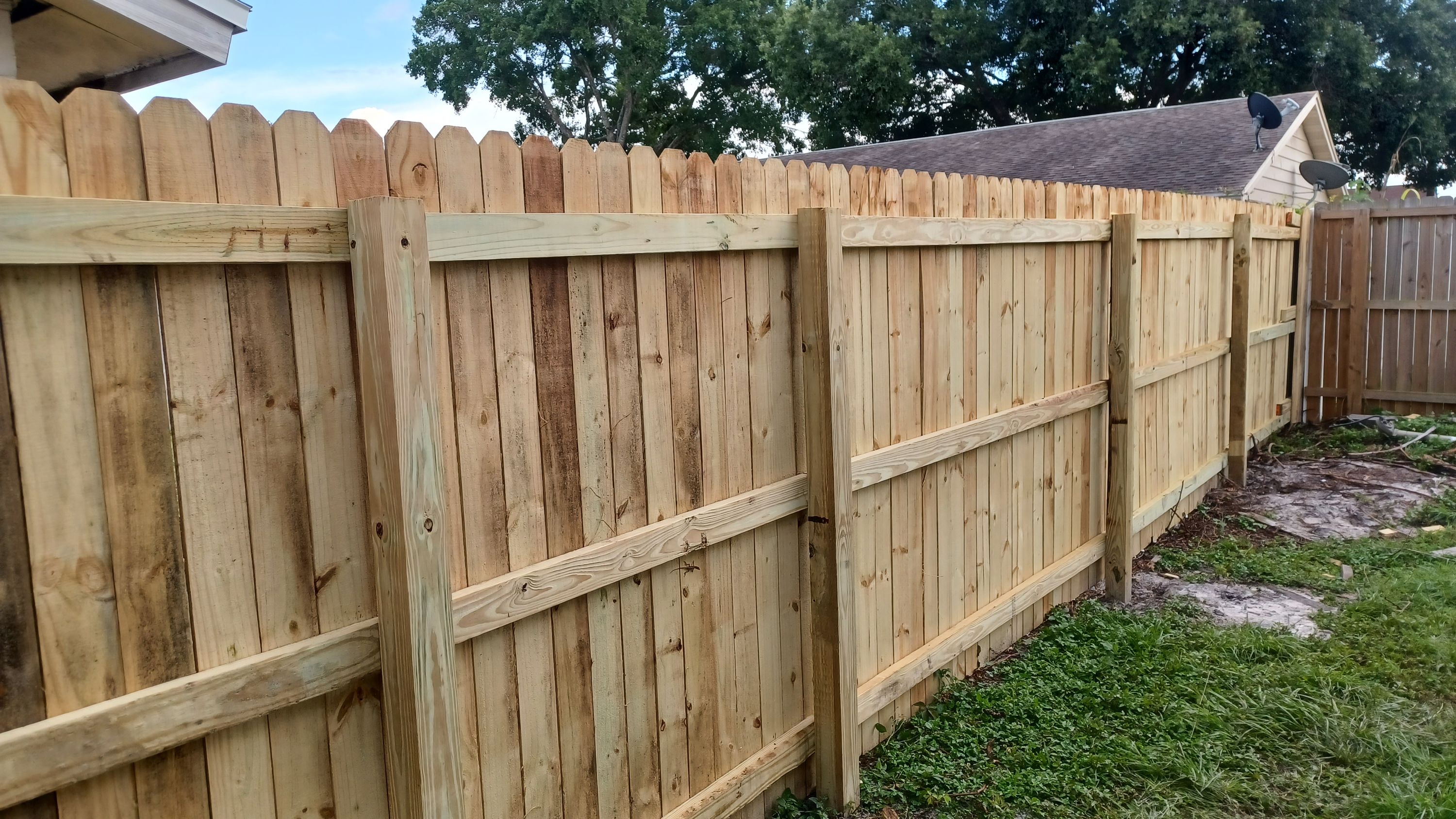 A tall dog-ear wood privacy fence built by Marquez Yera Fence, rails and posts square in full sun