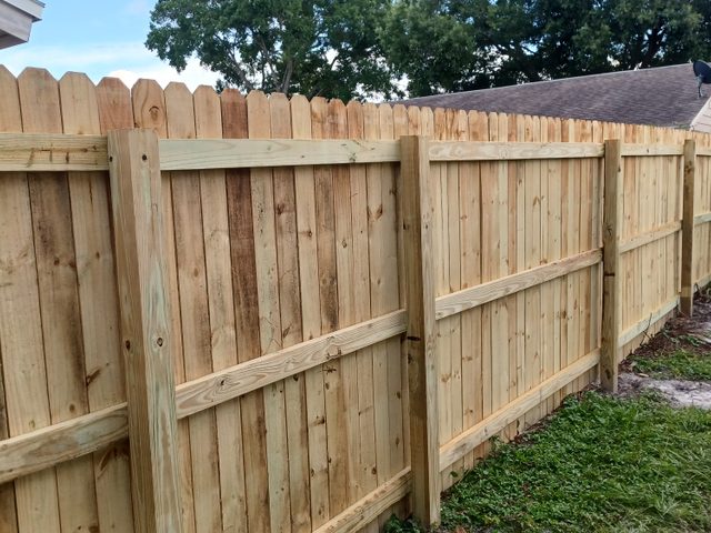 A tall dog-ear wood privacy fence built by Marquez Yera Fence, rails and posts square in full sun