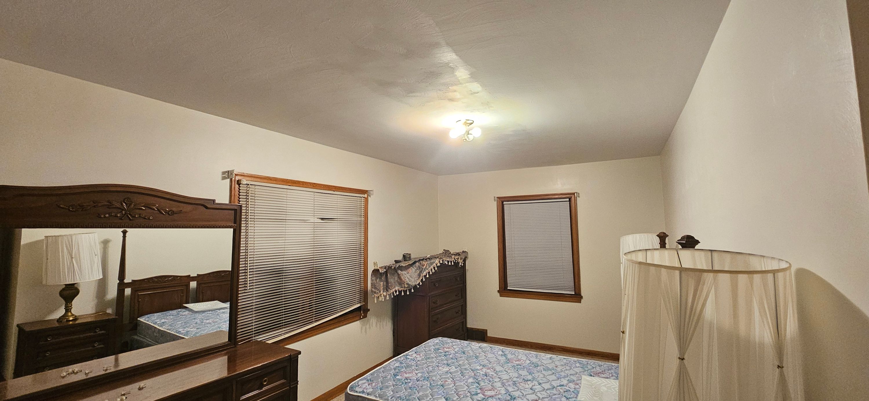 Furnished bedroom before painting with dated cream walls, dresser, mirror and bed in place