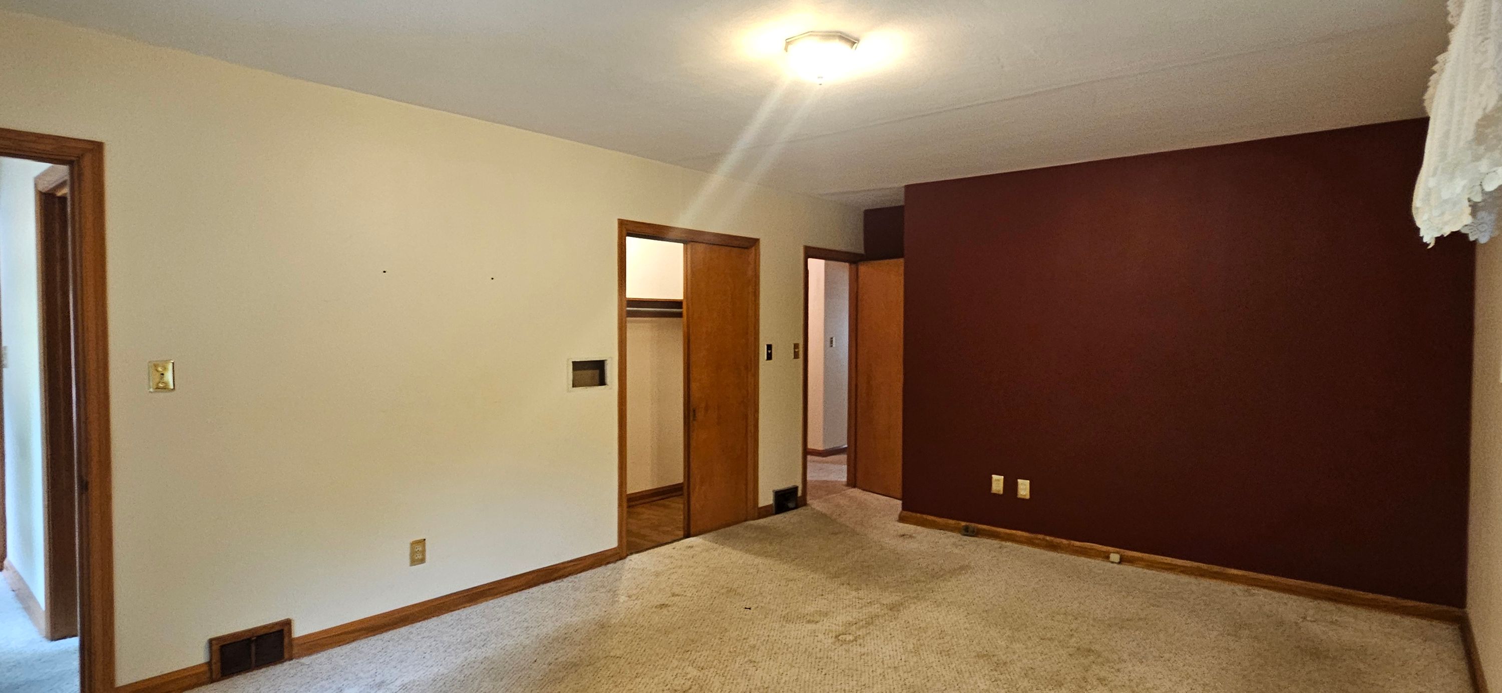 Empty bedroom before work, showing a dark maroon accent wall beside cream walls