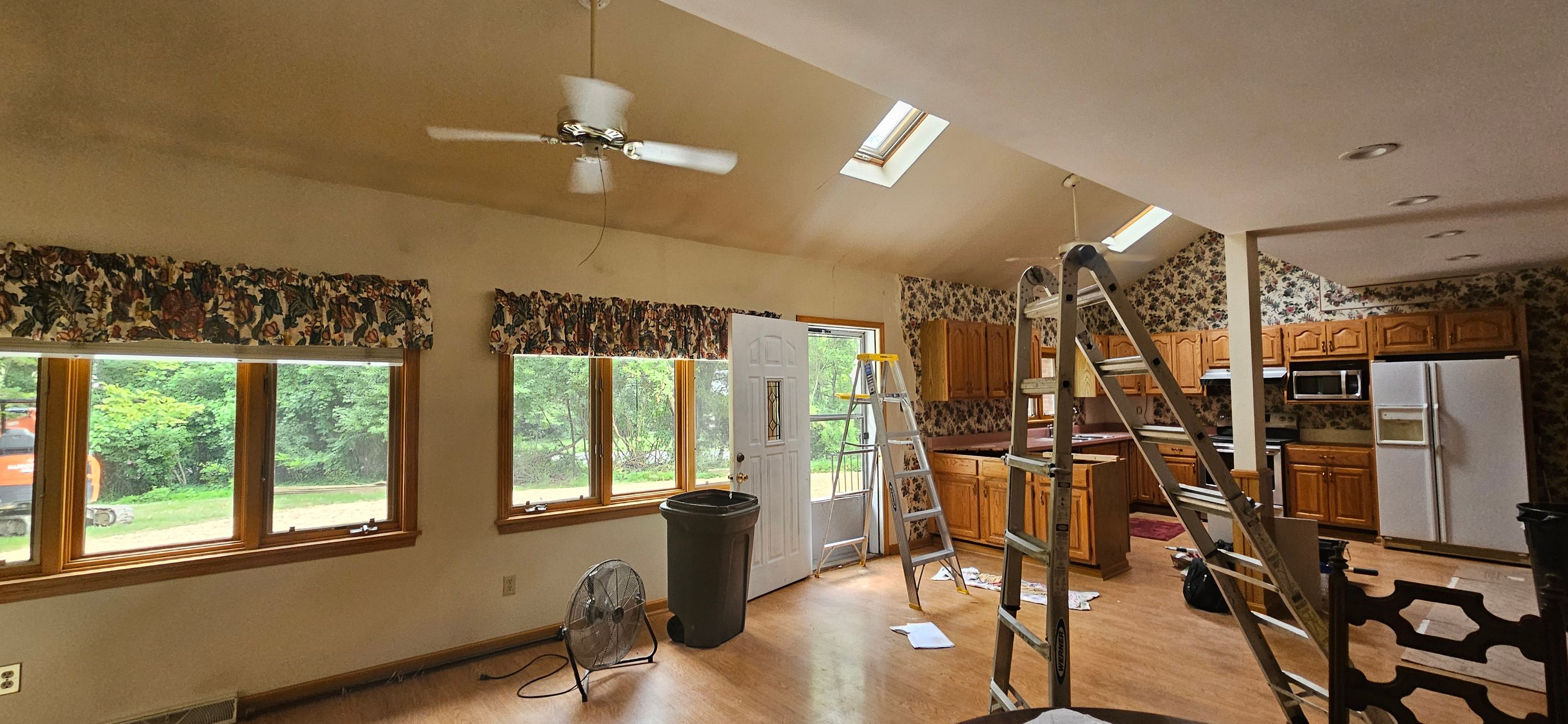 Living and kitchen area during prep with ladders, drop sheets and tan walls awaiting paint
