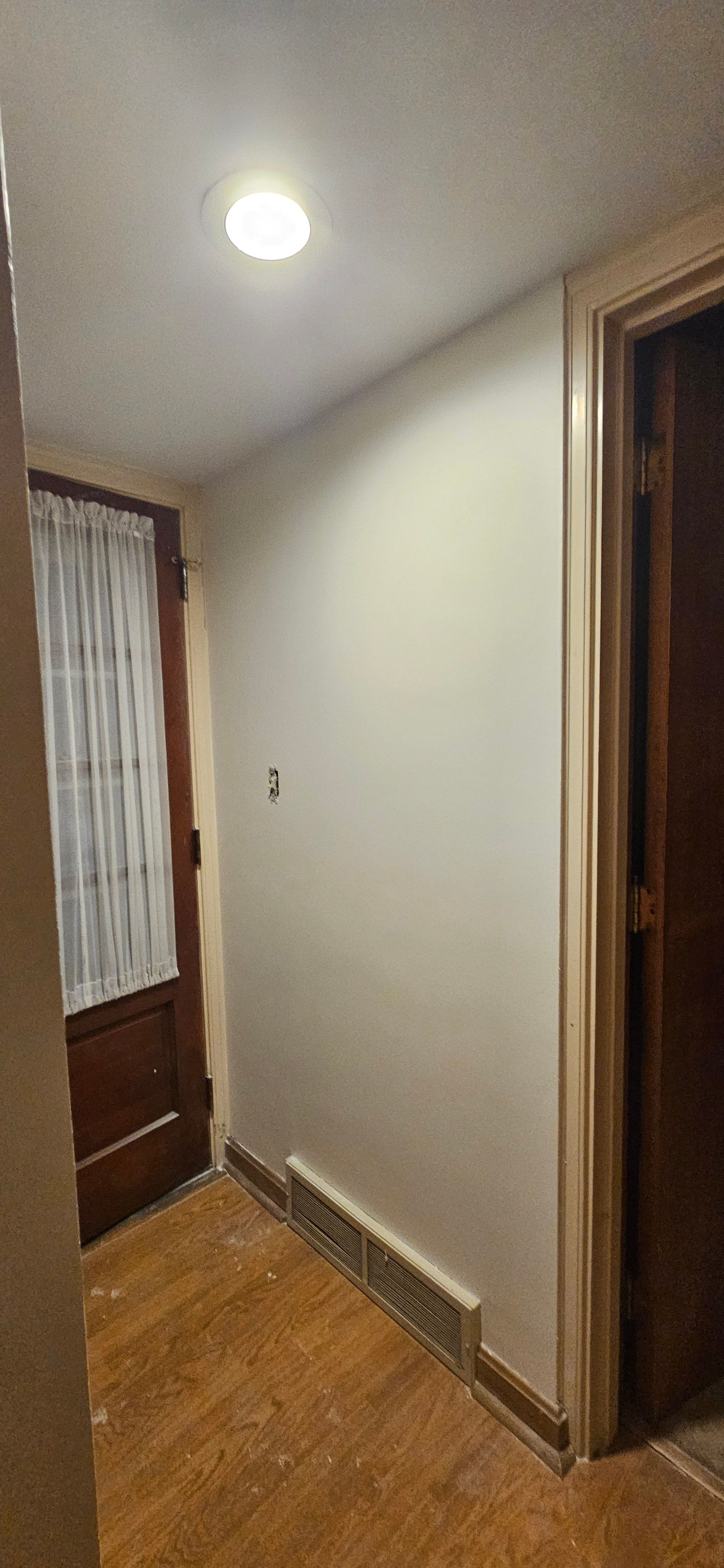 Narrow entry hallway with freshly painted pale walls, a dark wood door and hardwood floor