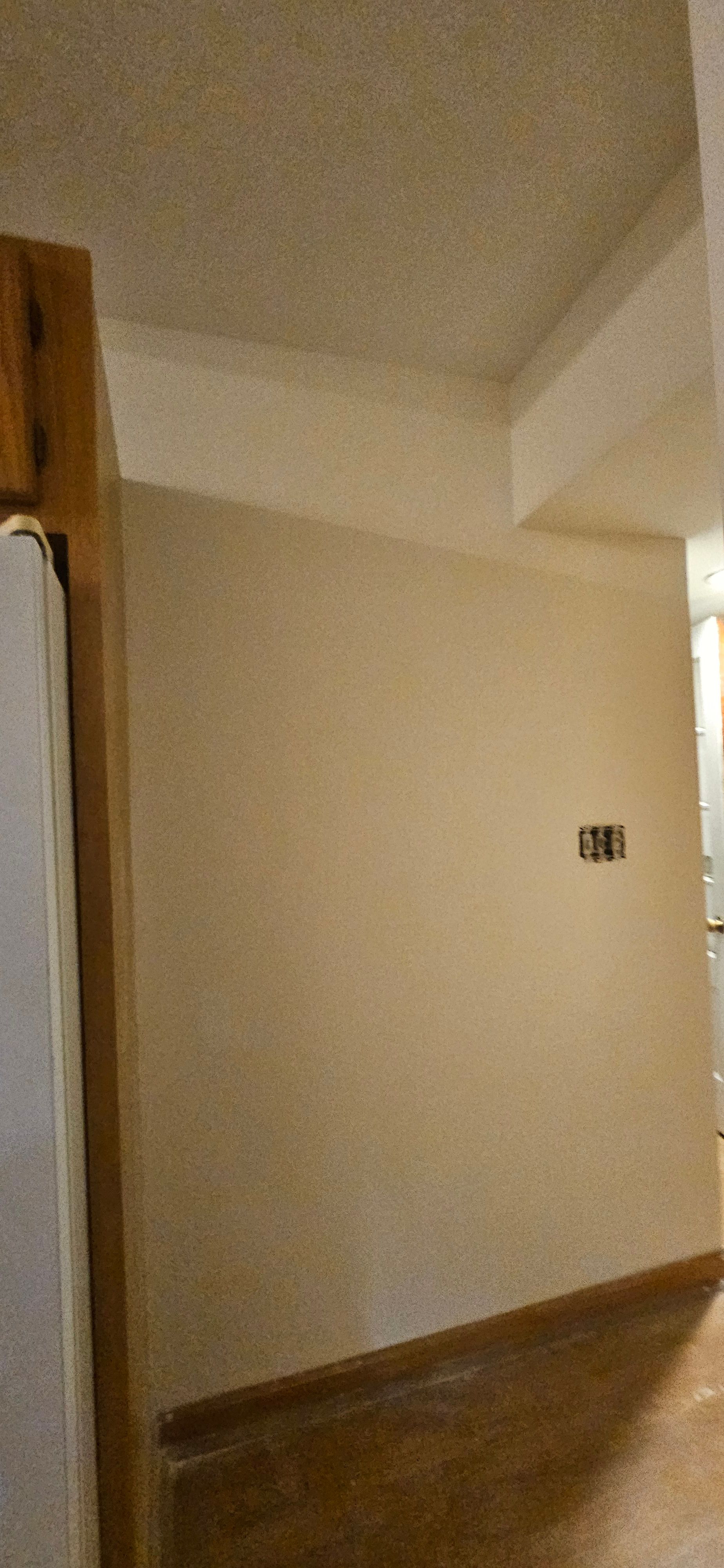 Interior corner wall coated in warm beige next to wood trim and a textured ceiling