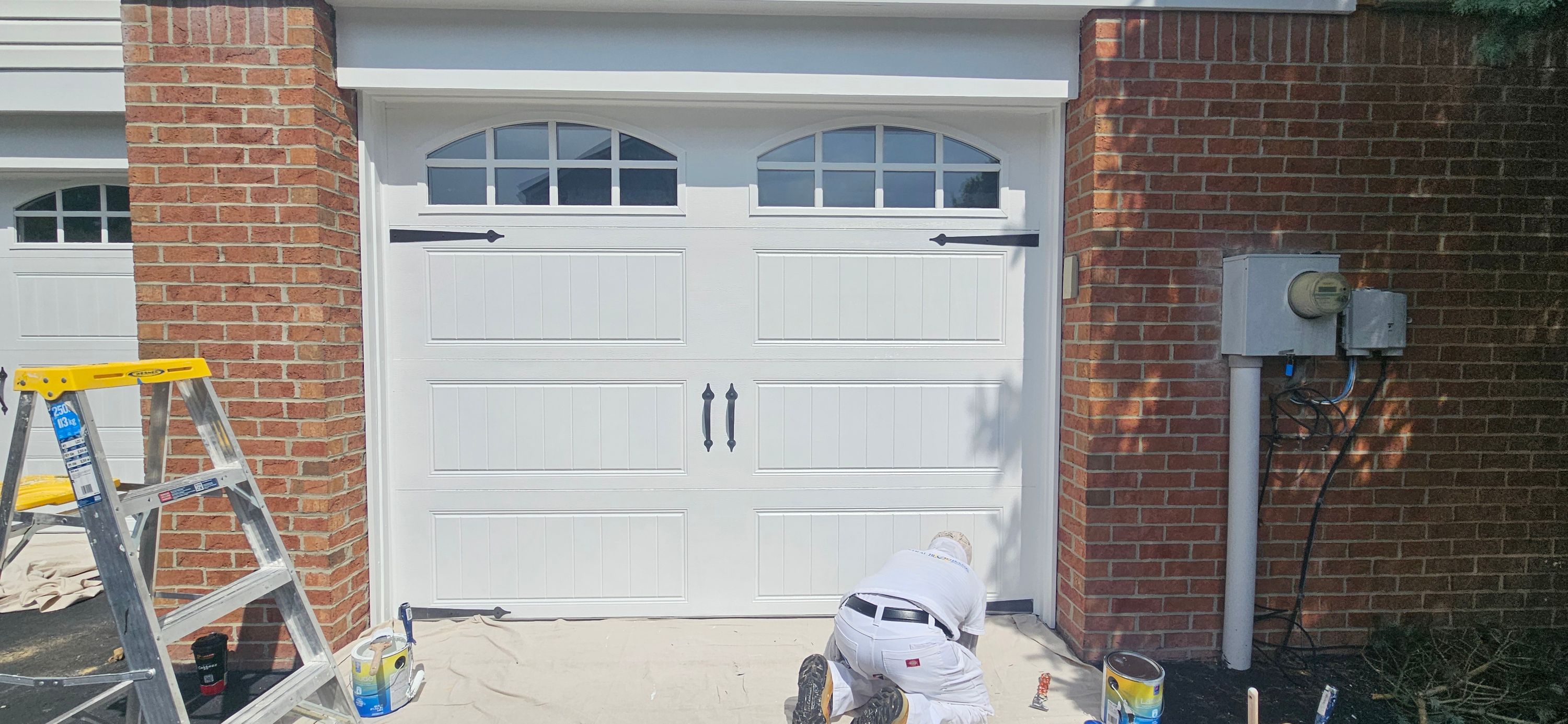 Painter kneeling on drop cloths cutting in white trim around a garage door opening
