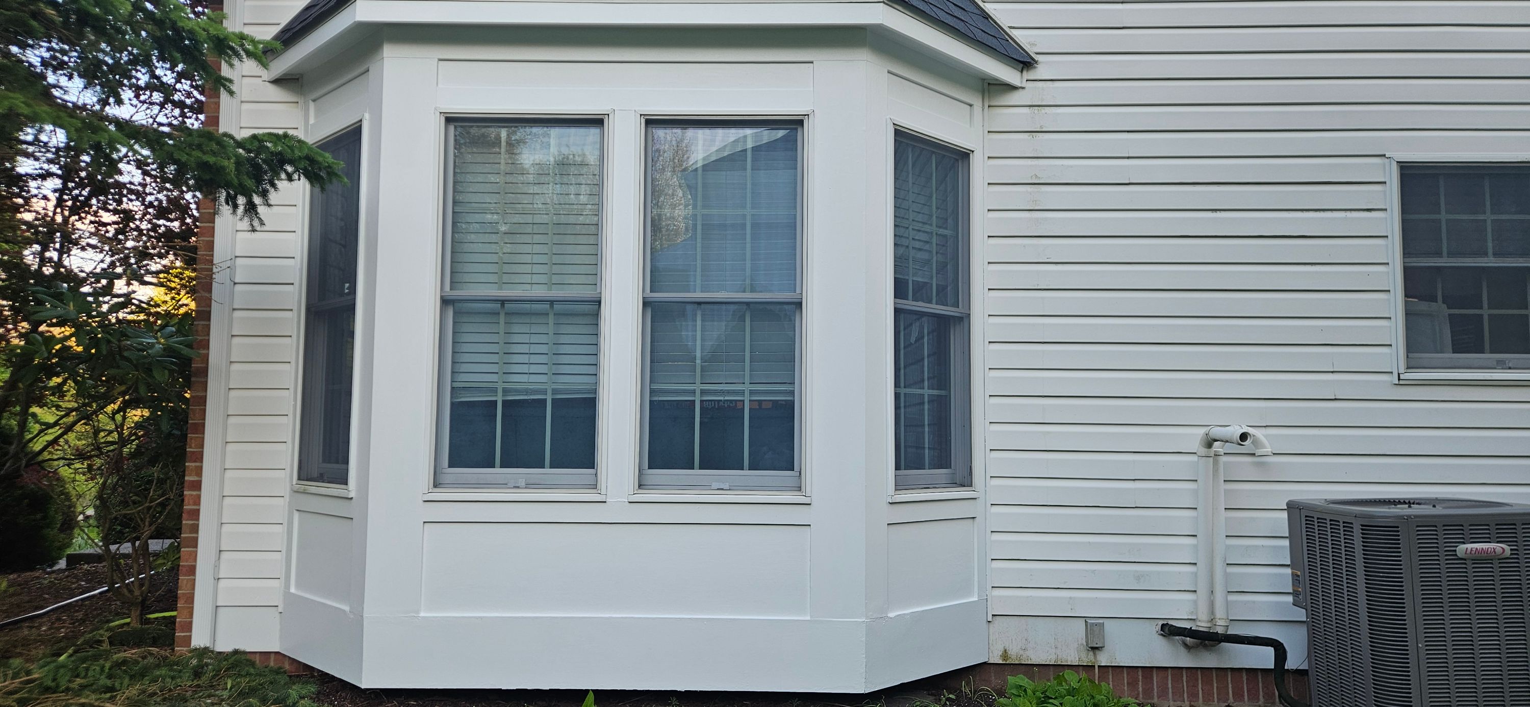 Bay window with crisp white trim and casing against white lap siding, exterior repaint complete