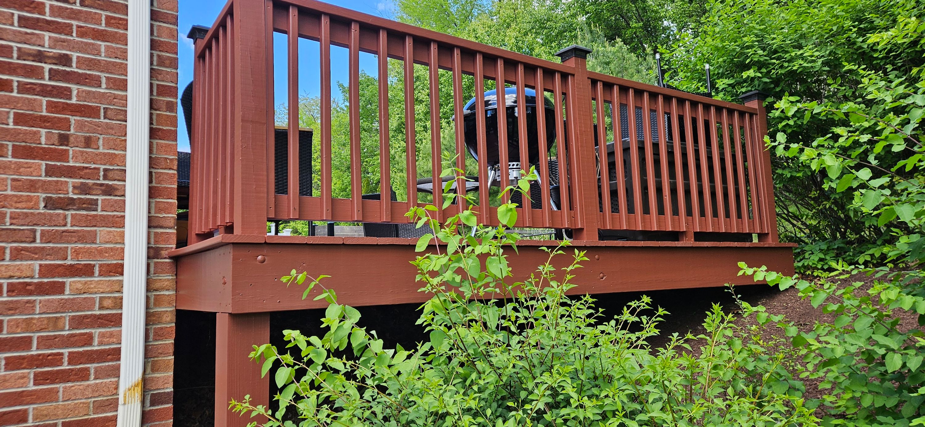 Raised wooden deck railing restained deep reddish brown beside a red brick house wall