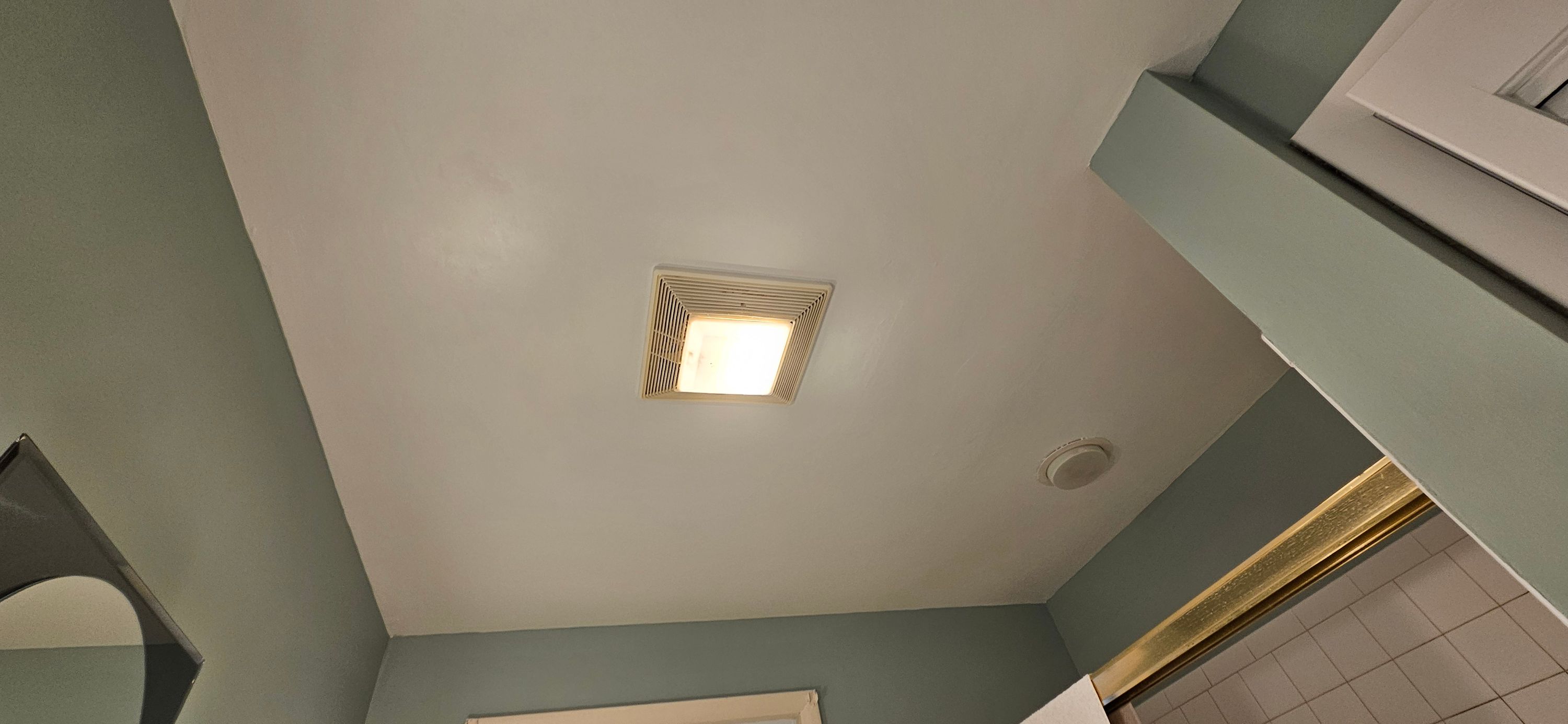 Bathroom ceiling repainted flat white meeting teal-green walls near a lit exhaust fan
