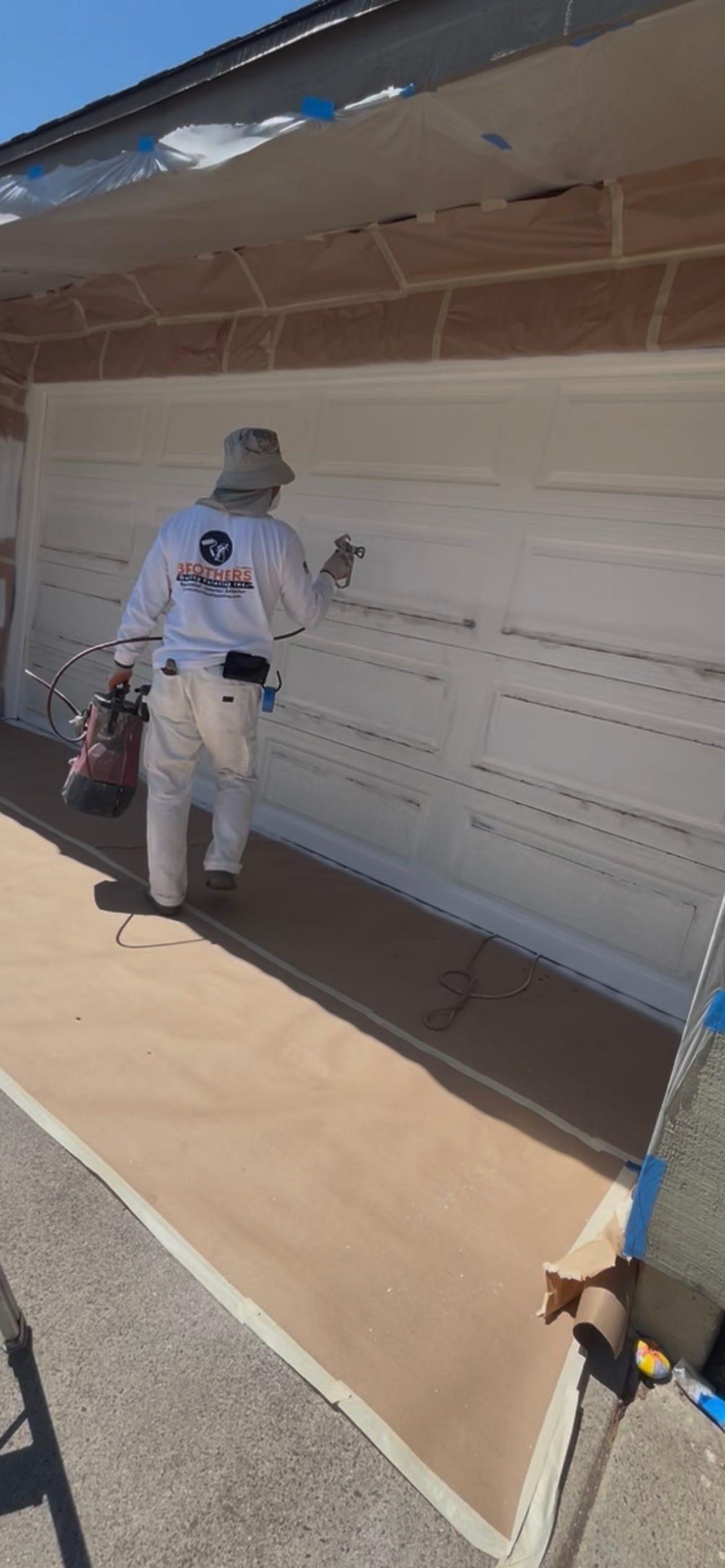 Brothers Quality Painting crew member spray-painting a garage door with the floor fully masked