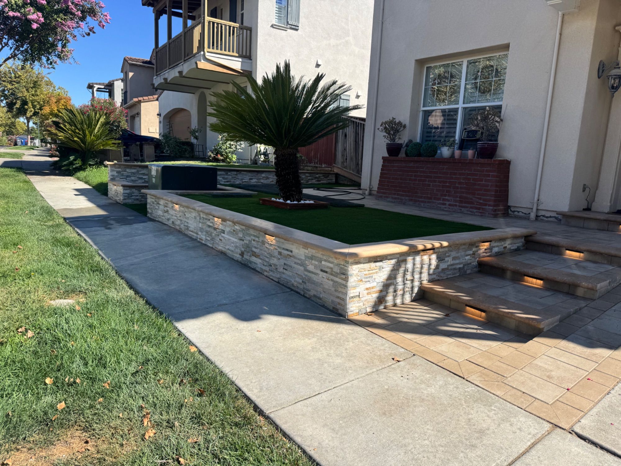 Stone planter wall with turf and paver steps at a front entry