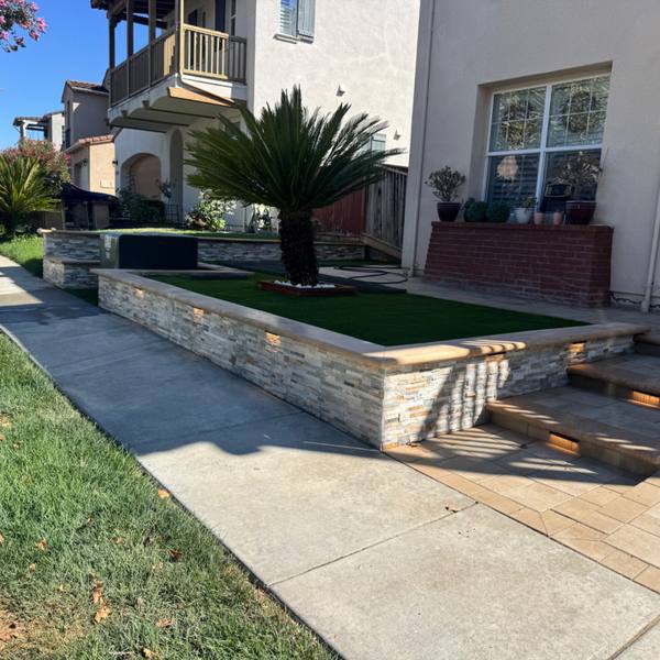 Stone planter wall with turf and paver steps at a front entry