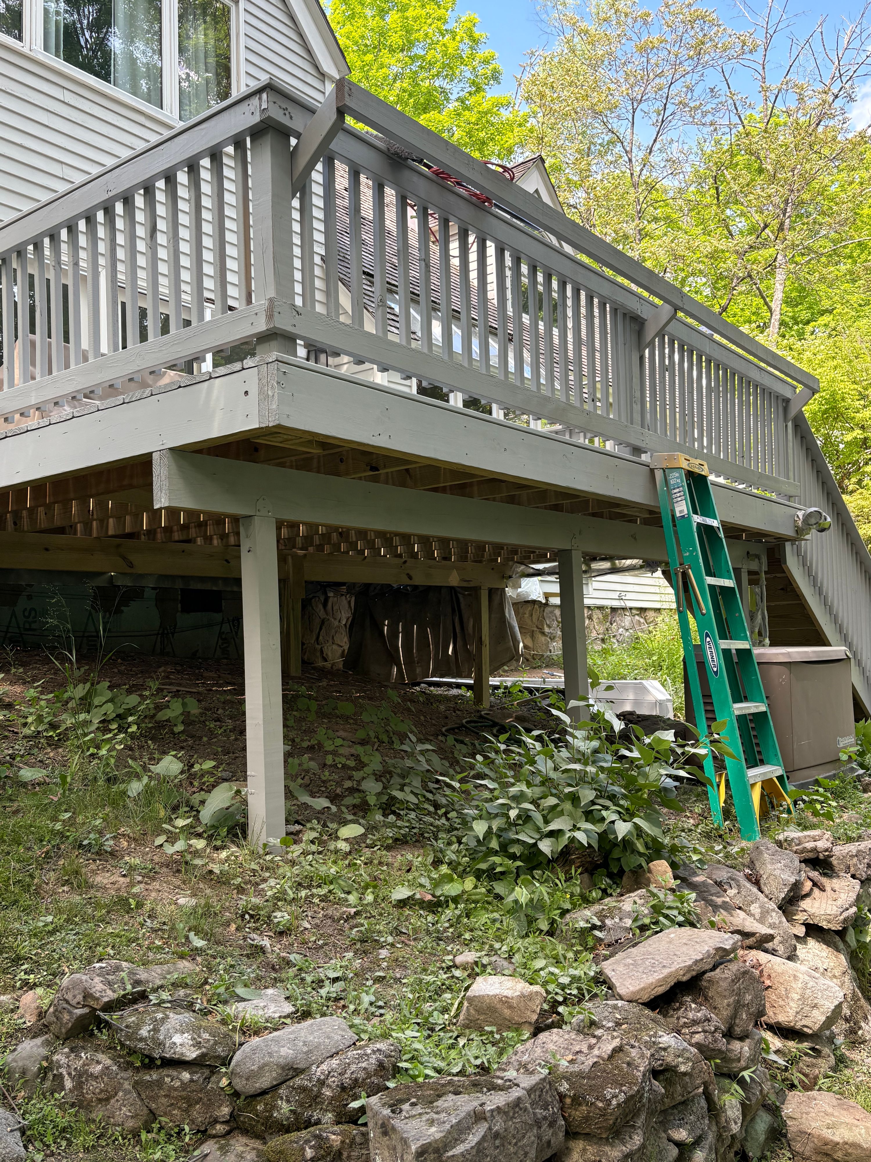 Underside of a raised deck after painting, with a ladder set up on the slope below — FE Pro Painting