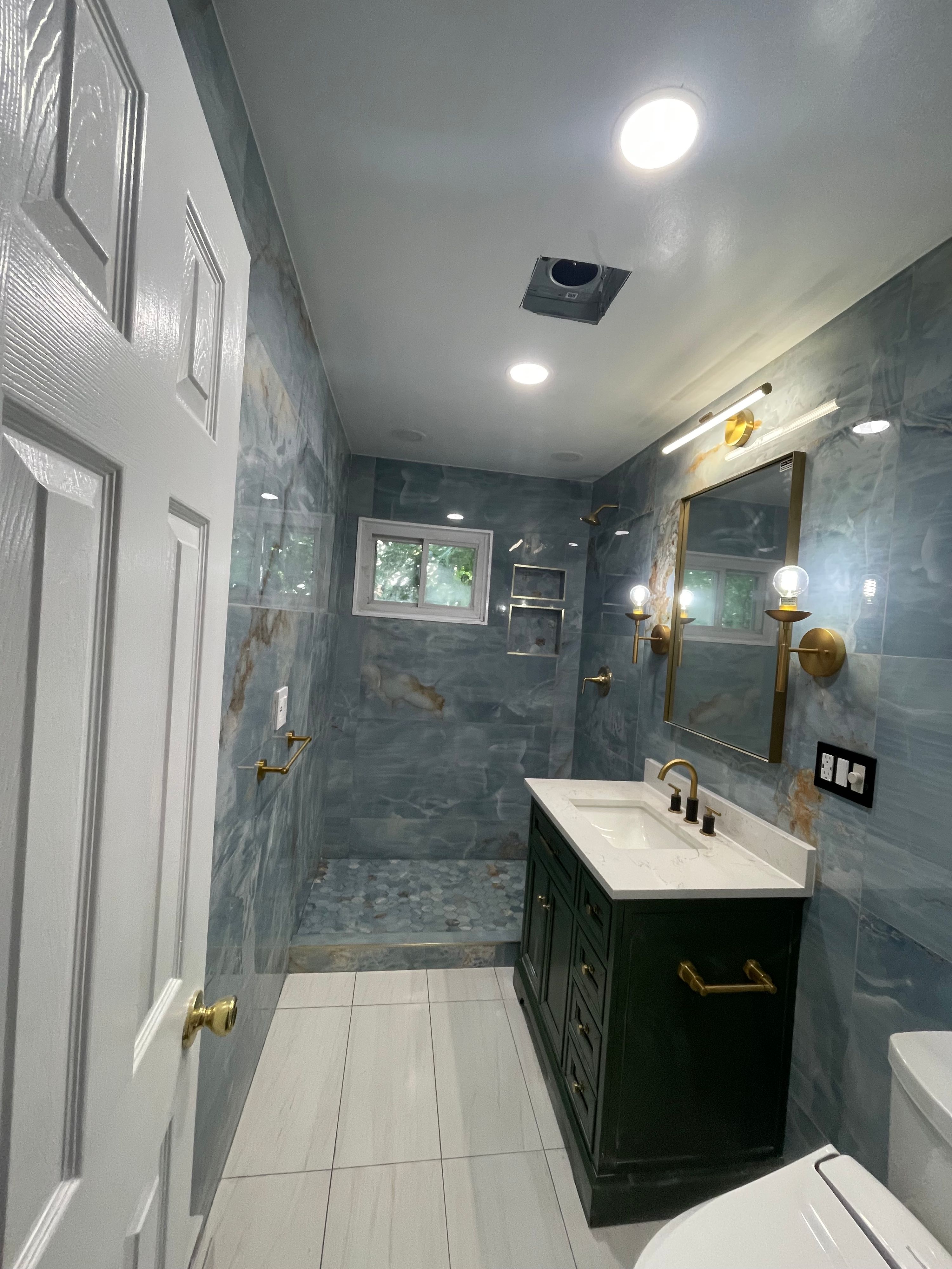Bathroom with blue-grey marble-effect tiling, a dark vanity unit and brass fittings — FE Pro Painting