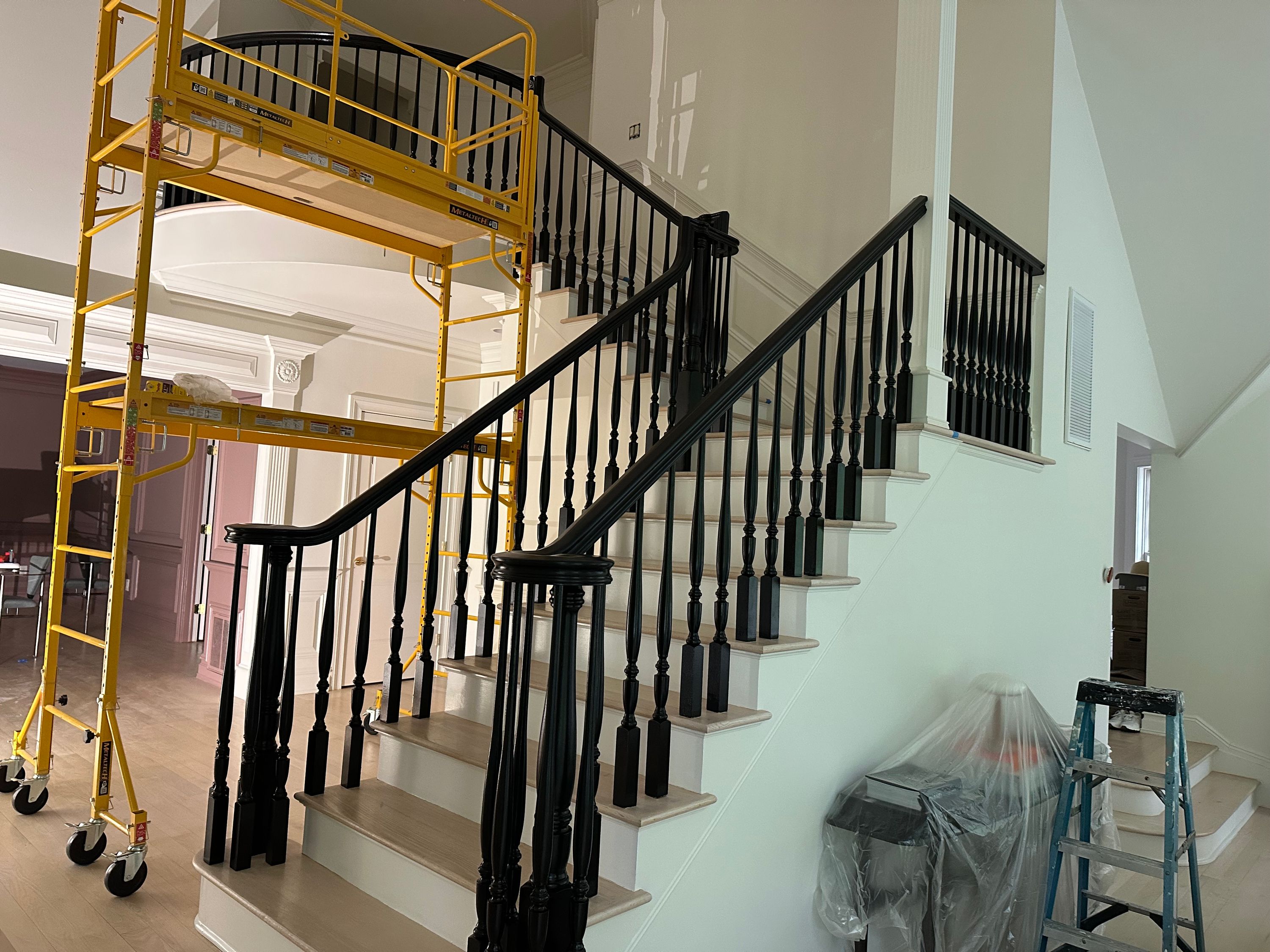 Interior staircase with freshly painted black balusters and handrail, scaffolding still in place — FE Pro Painting