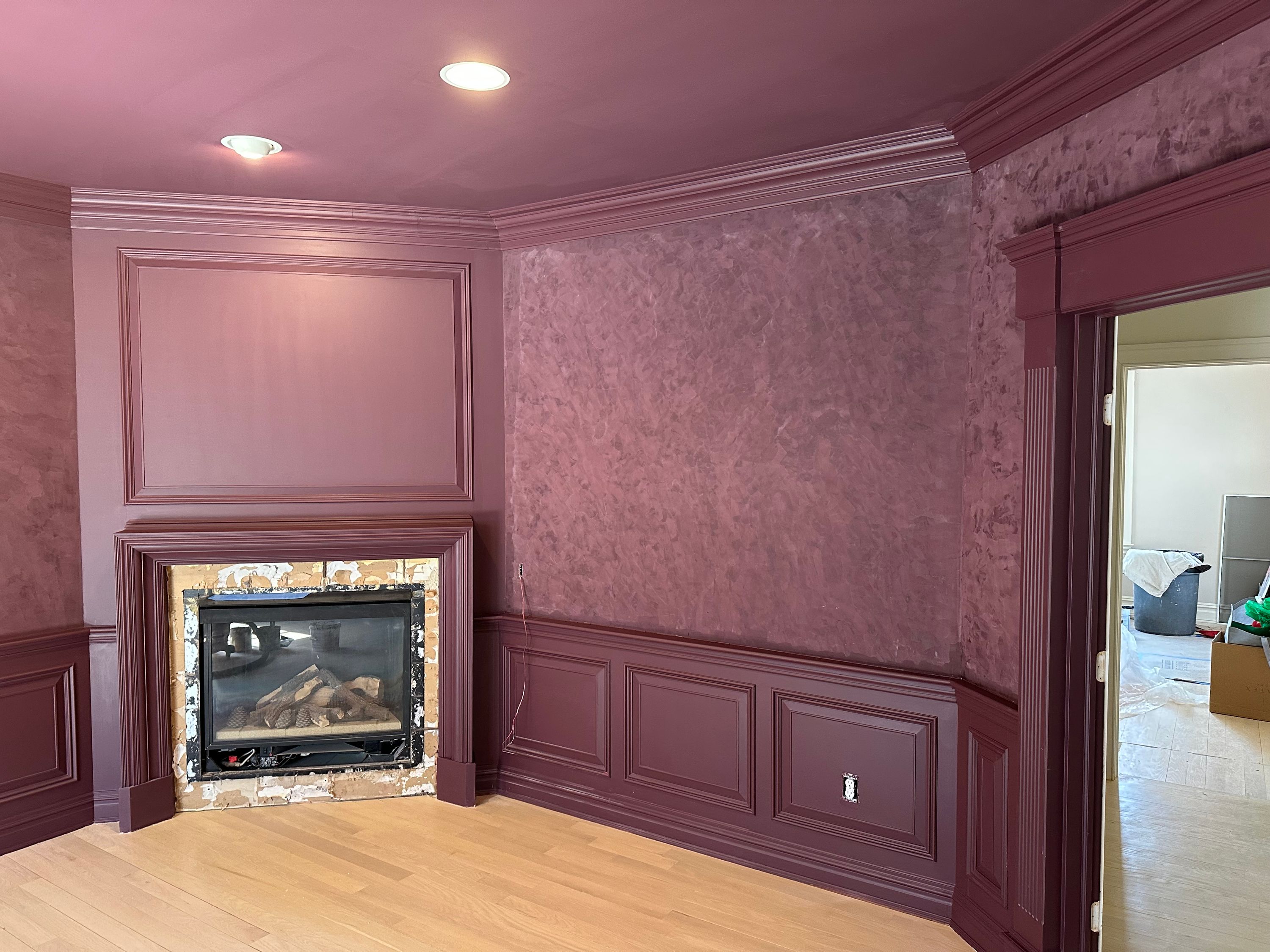 Living room finished in a deep plum, with painted wainscoting, crown moulding and a tiled fireplace surround — FE Pro Painting