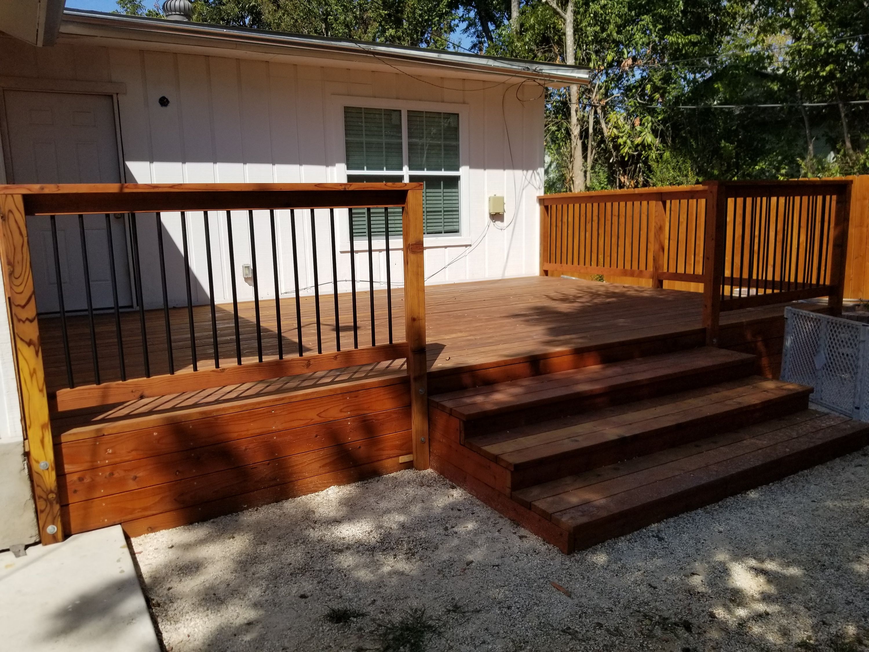 Finished redwood deck with black metal railing and steps beside a house