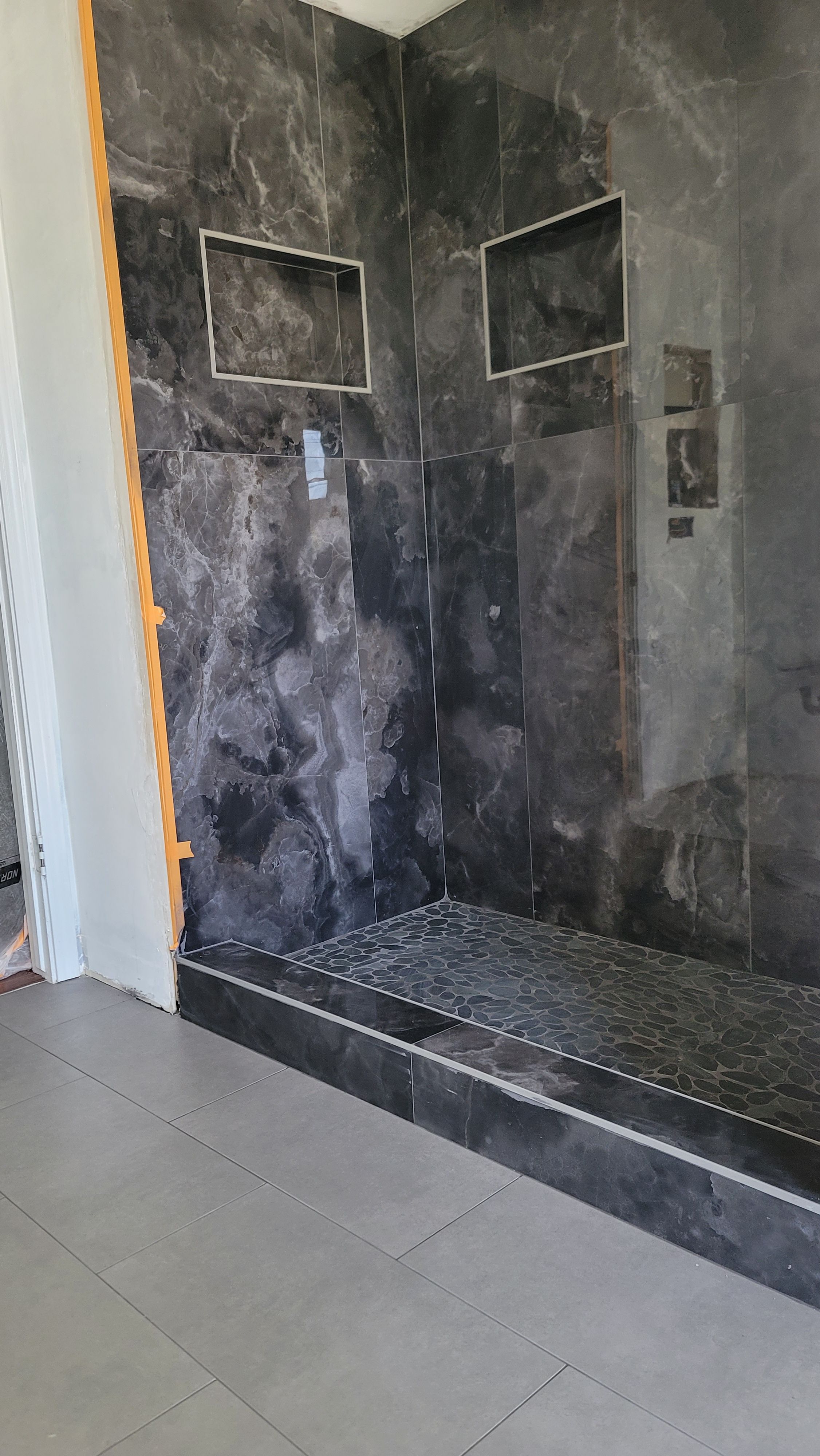 Dark marble tile shower surround with a tiled step, mid-installation