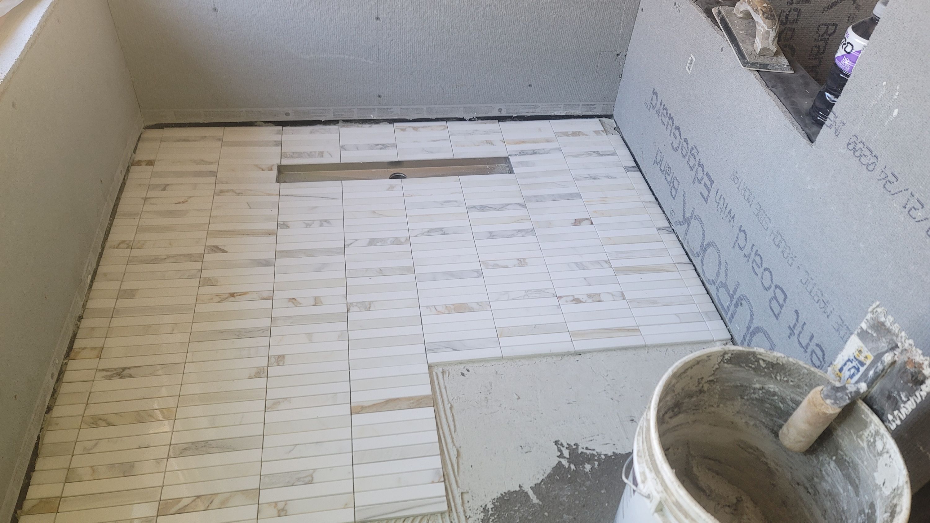 Pale rectangular floor tile being laid across a bathroom floor