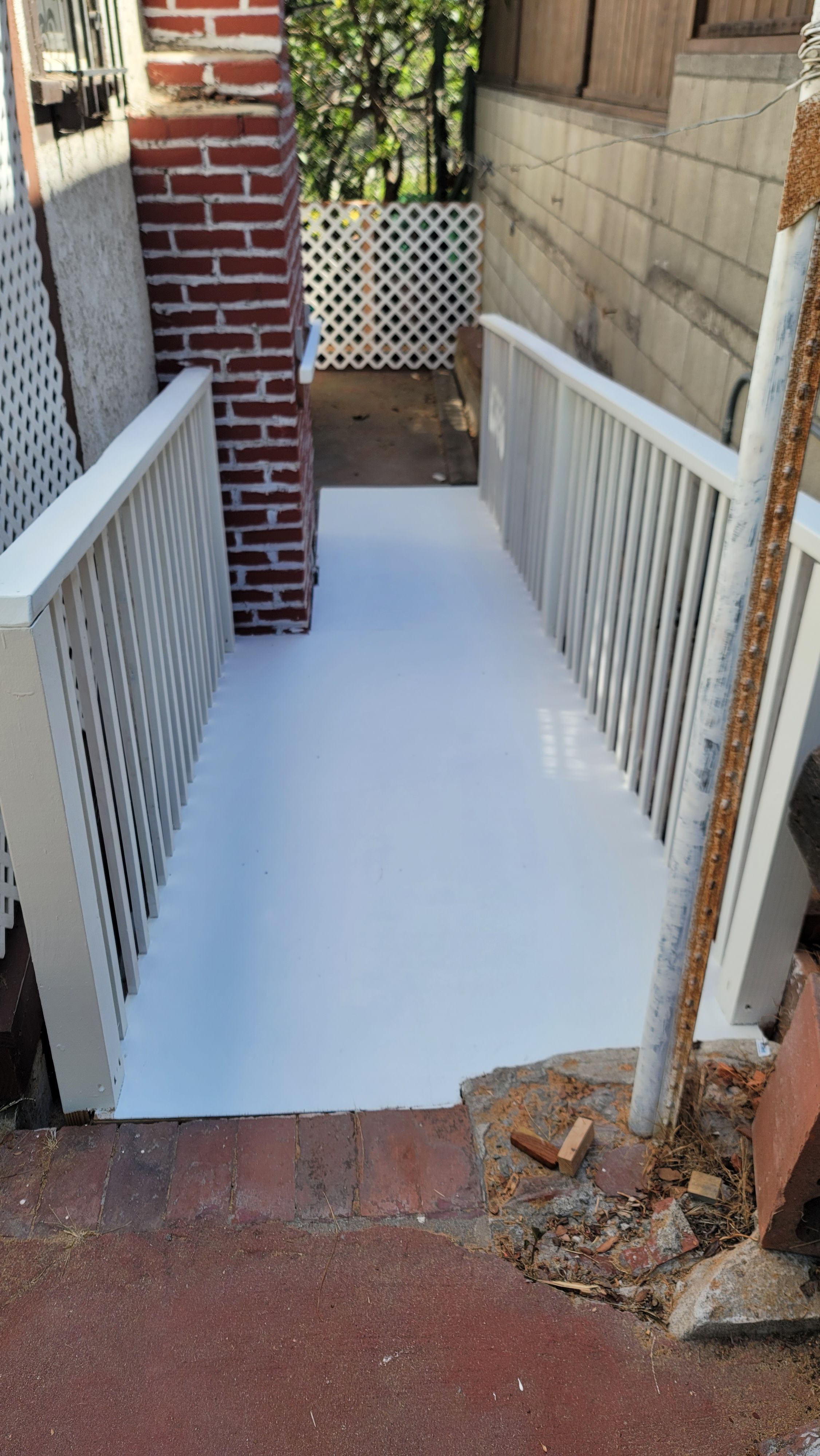 Coated concrete walkway between white railings and a brick pillar