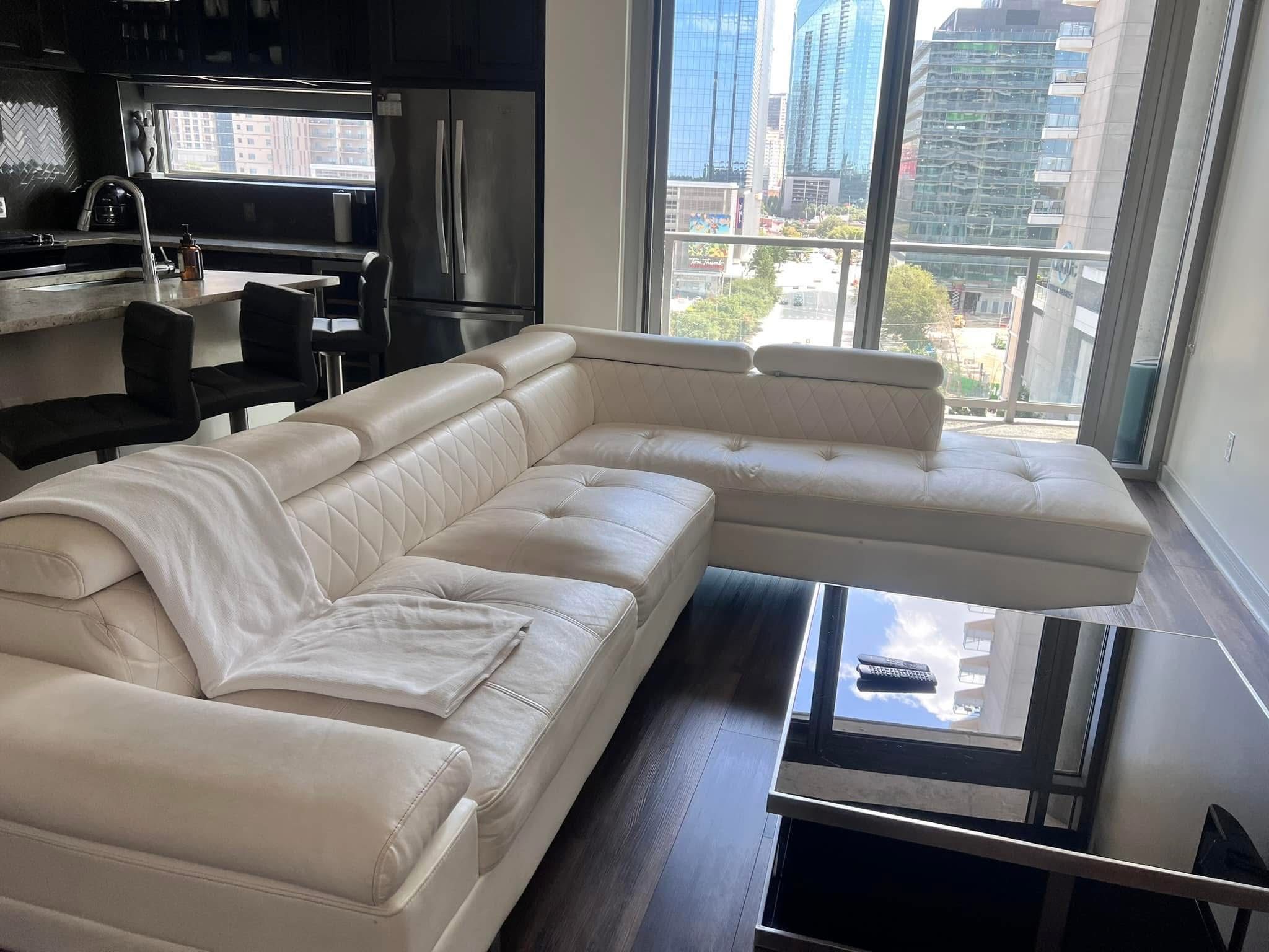 Bright living room with cleaned sectional sofa, floor, and glass table