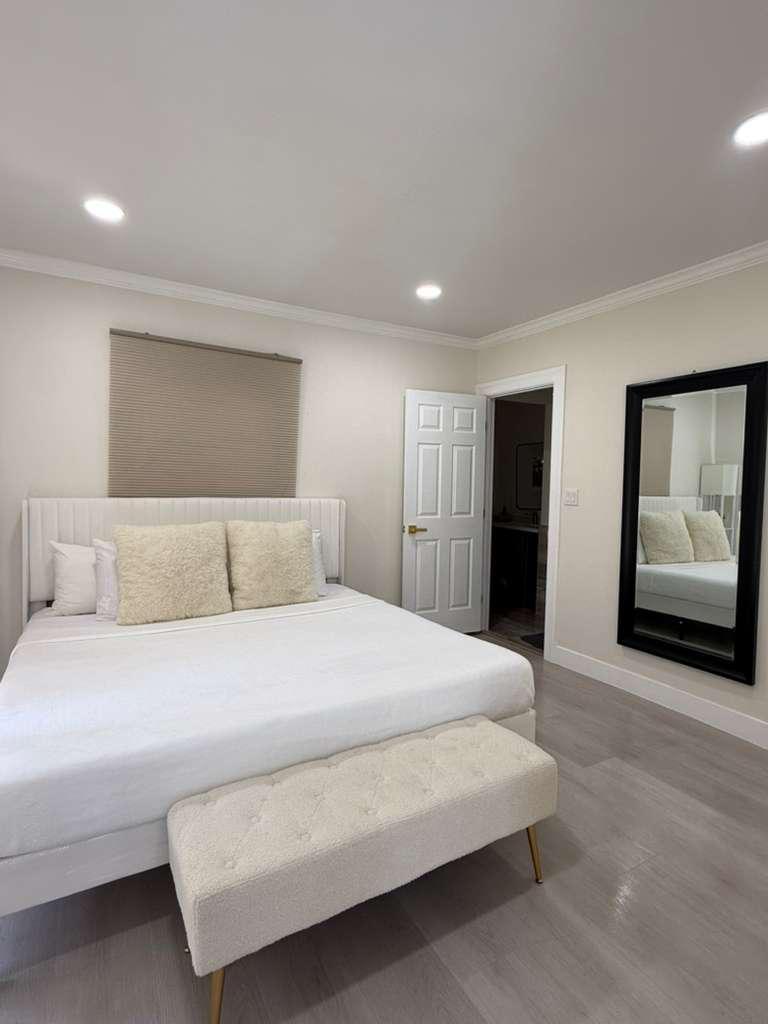 Bedroom with white bedding, an upholstered bench and a floor mirror