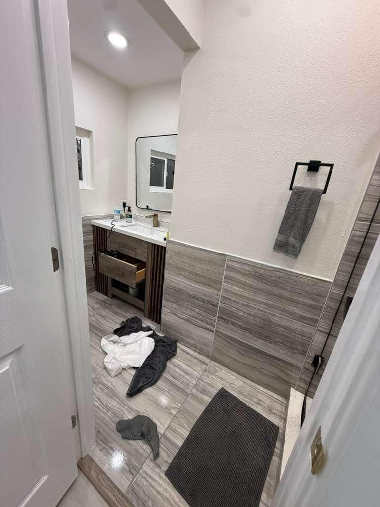 Bathroom before cleaning, with towels and clothes on the floor