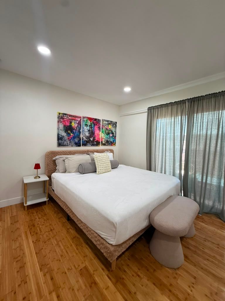 Bedroom with a made bed, colorful wall art and sheer curtains