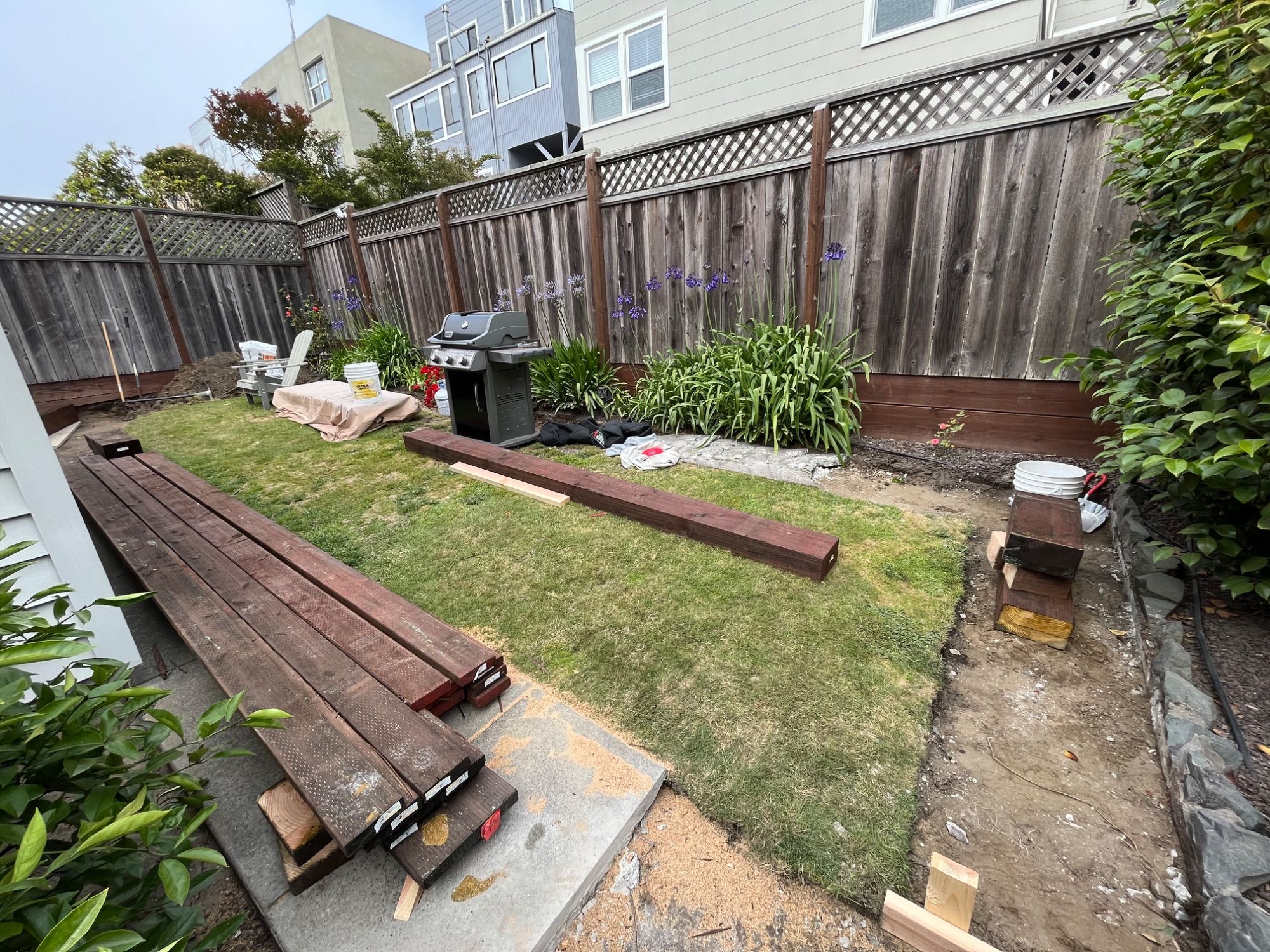 A back garden stripped out during demolition, with old deck timbers stacked across the lawn