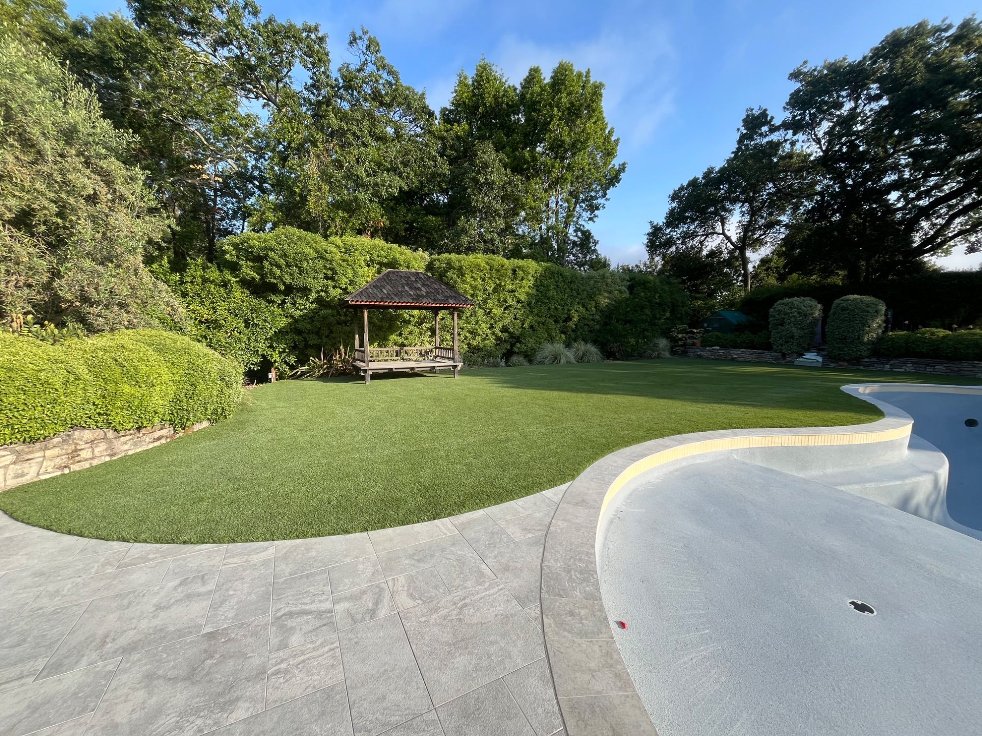 A large curved artificial turf lawn sweeping around a gazebo, edged against a concrete drive