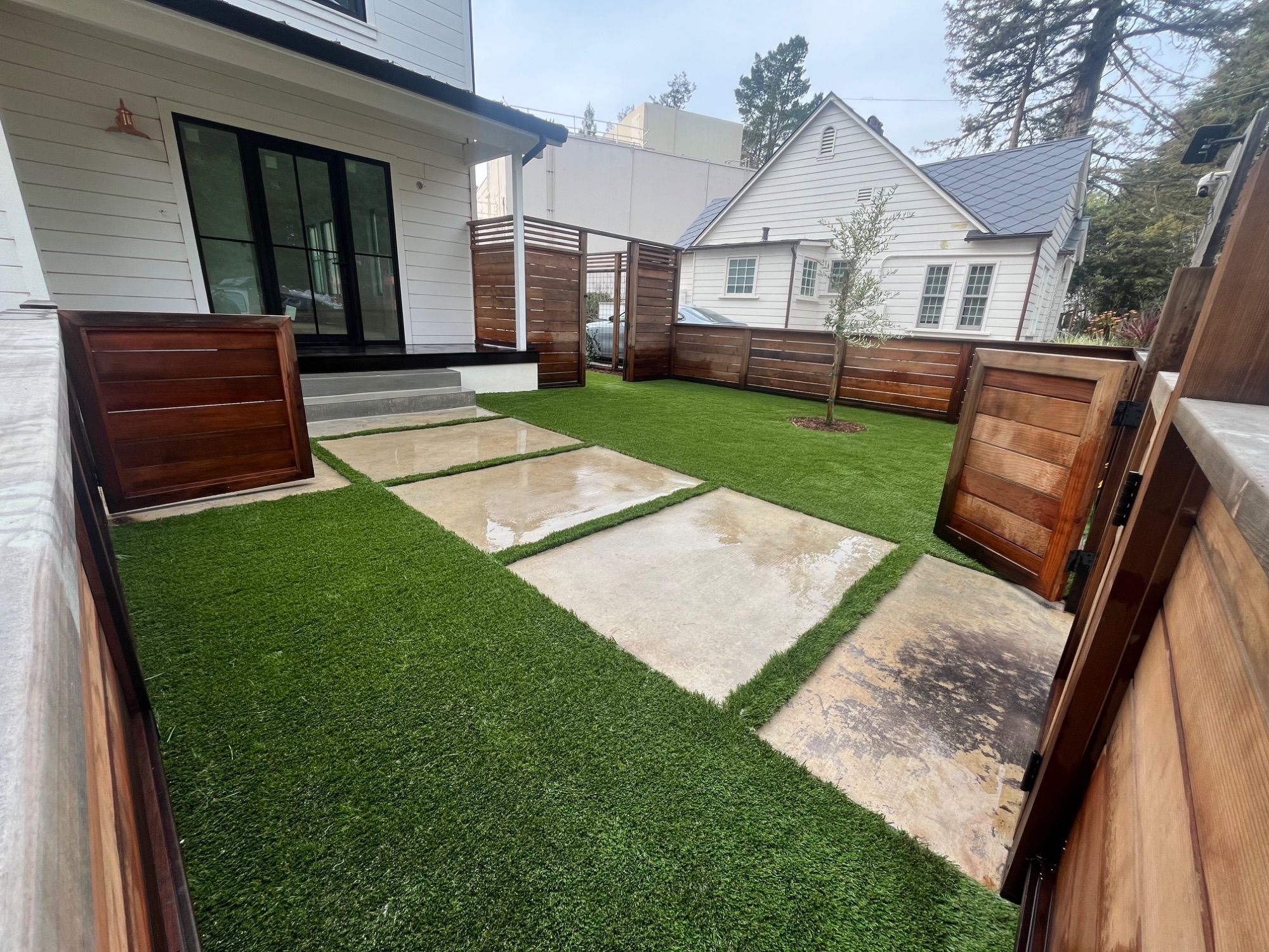 Artificial turf and concrete stepping pads laid in a small courtyard between hardwood screens