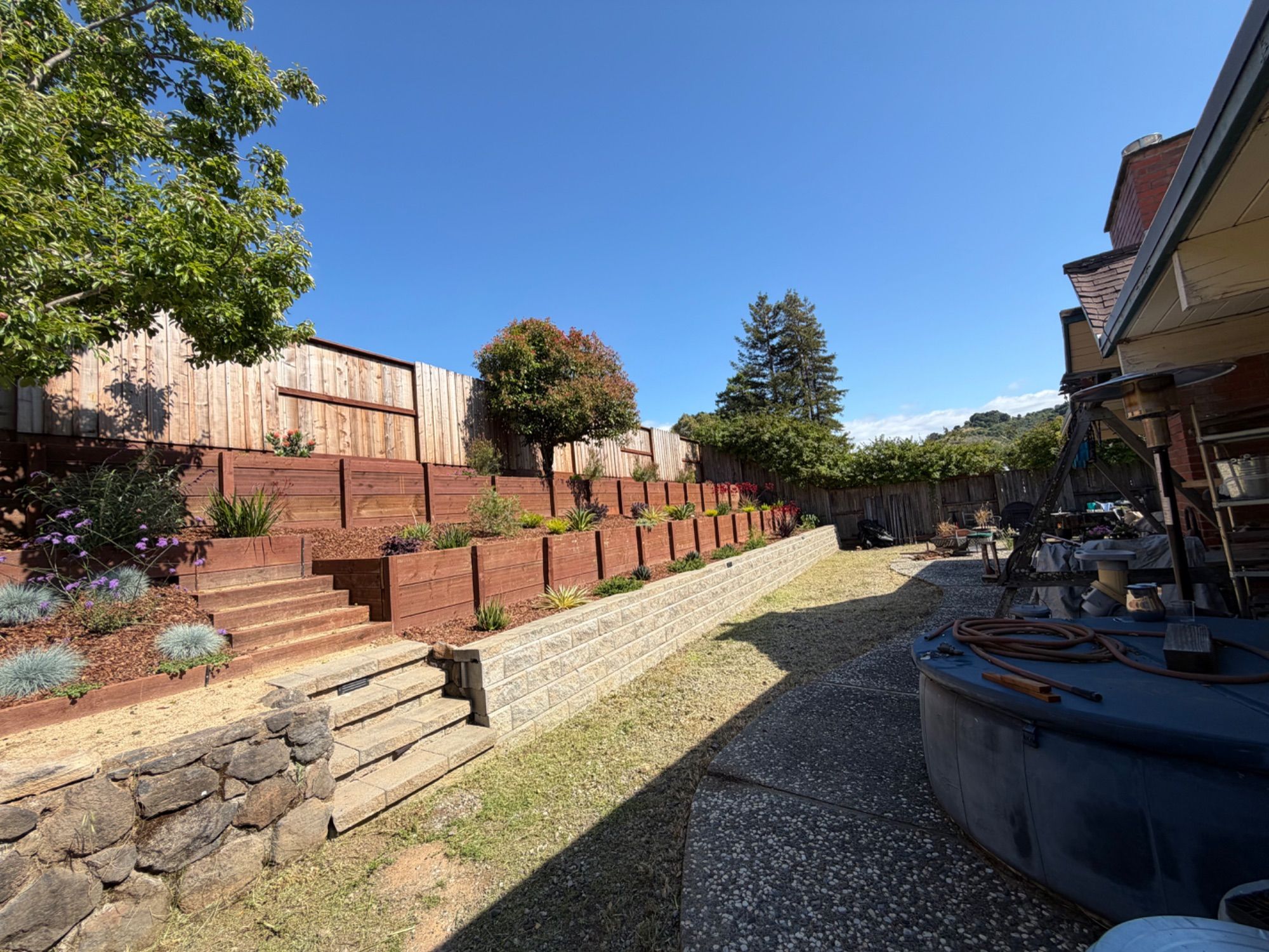 Timber retaining terraces stepping up a sunny back garden, with a gravel path along the house
