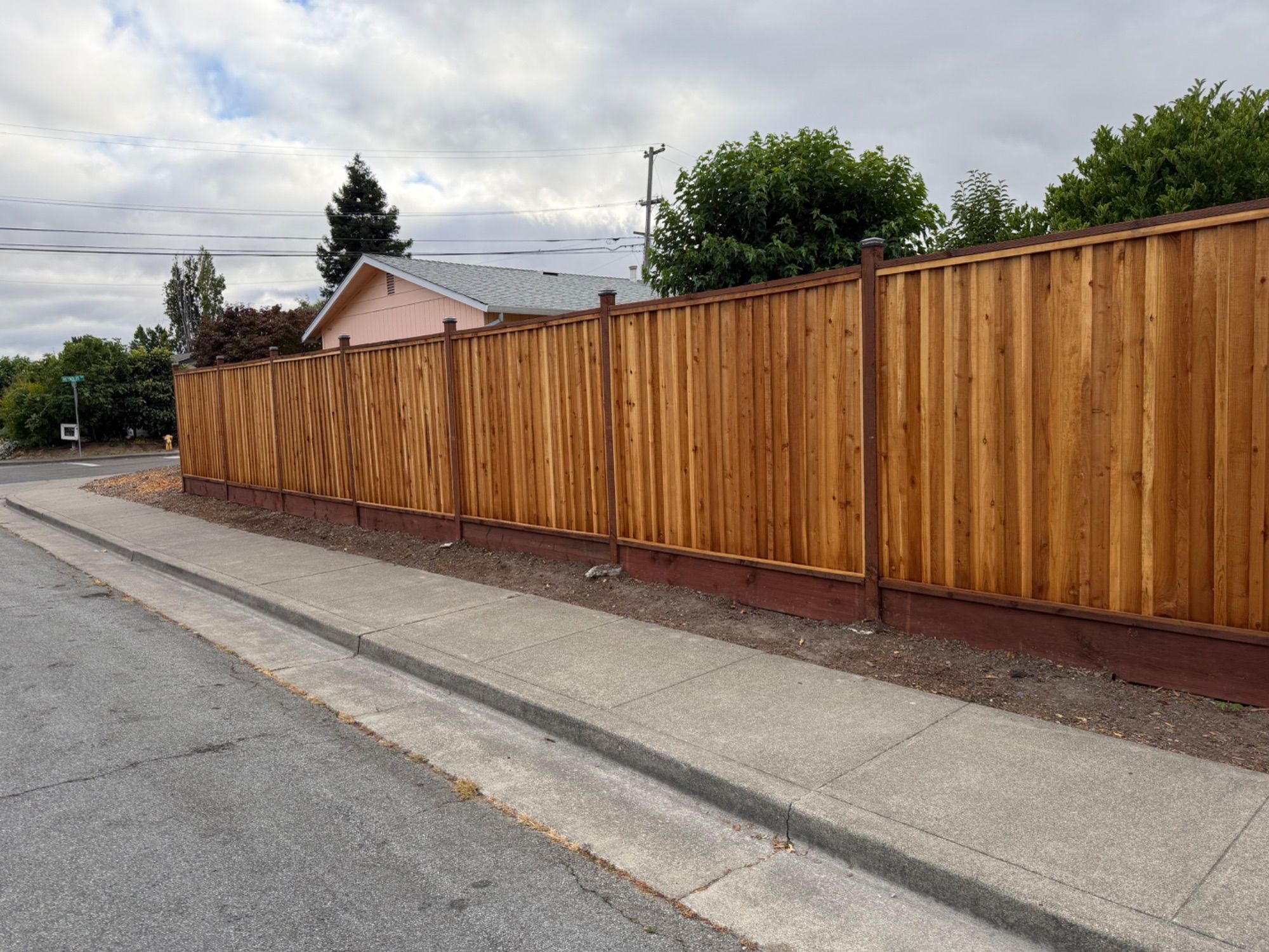 A long new redwood fence with a capped top rail running the length of a street frontage