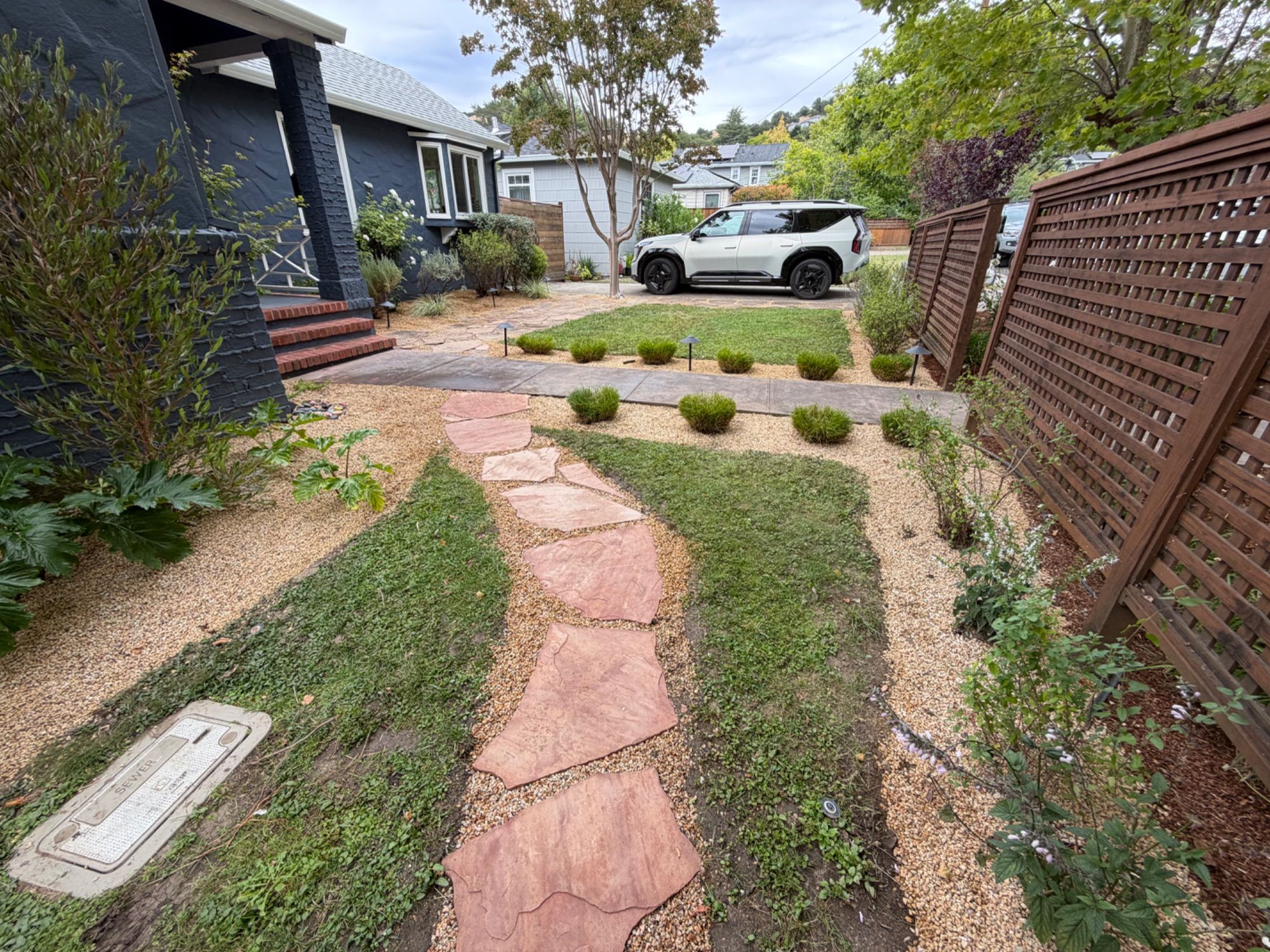 A front garden of flagstone stepping pads set into gravel and low planting, beside a slatted screen fence