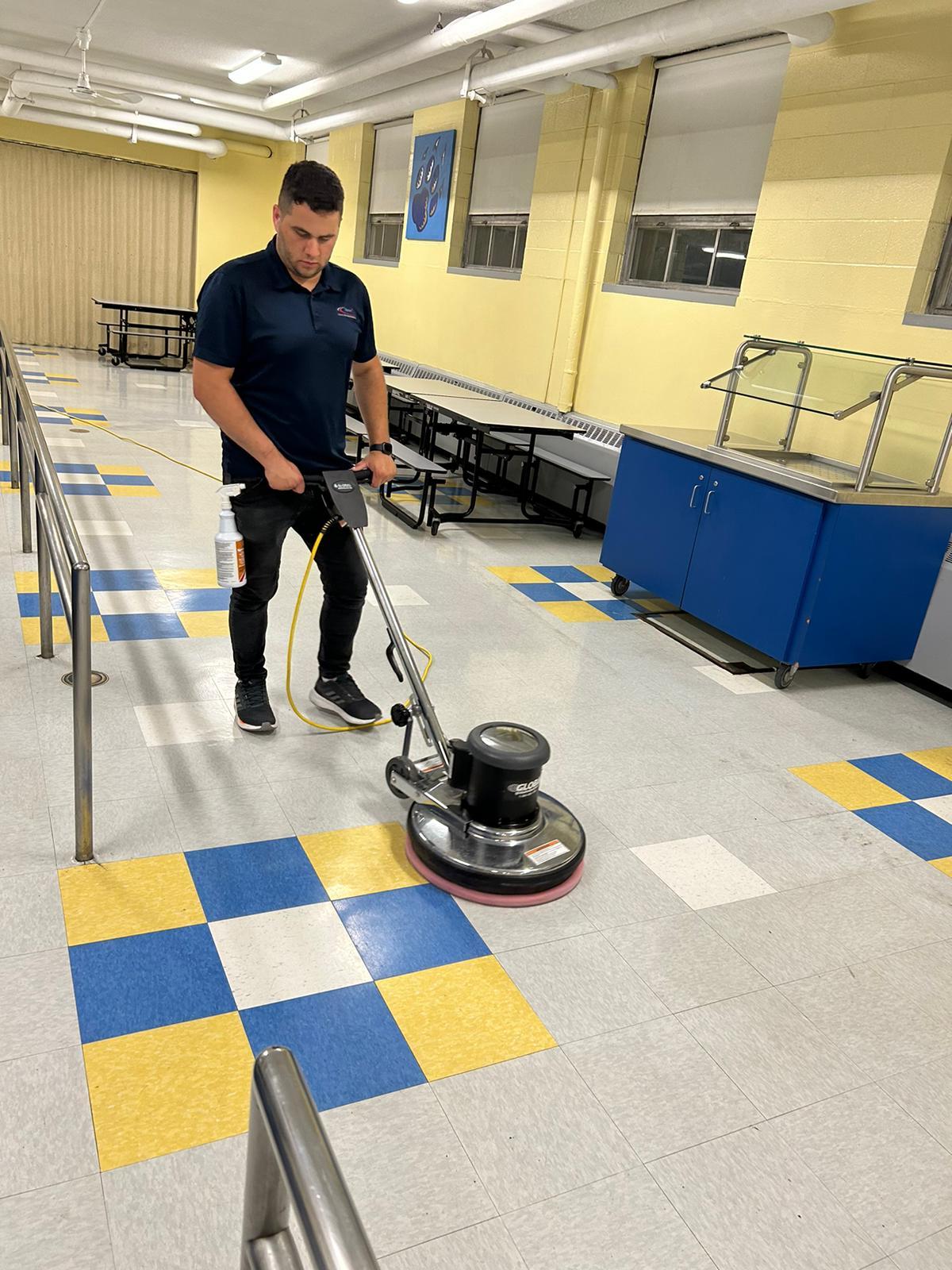 Miranda Shine Corp technician running a floor machine over blue and yellow VCT tile in a school cafeteria