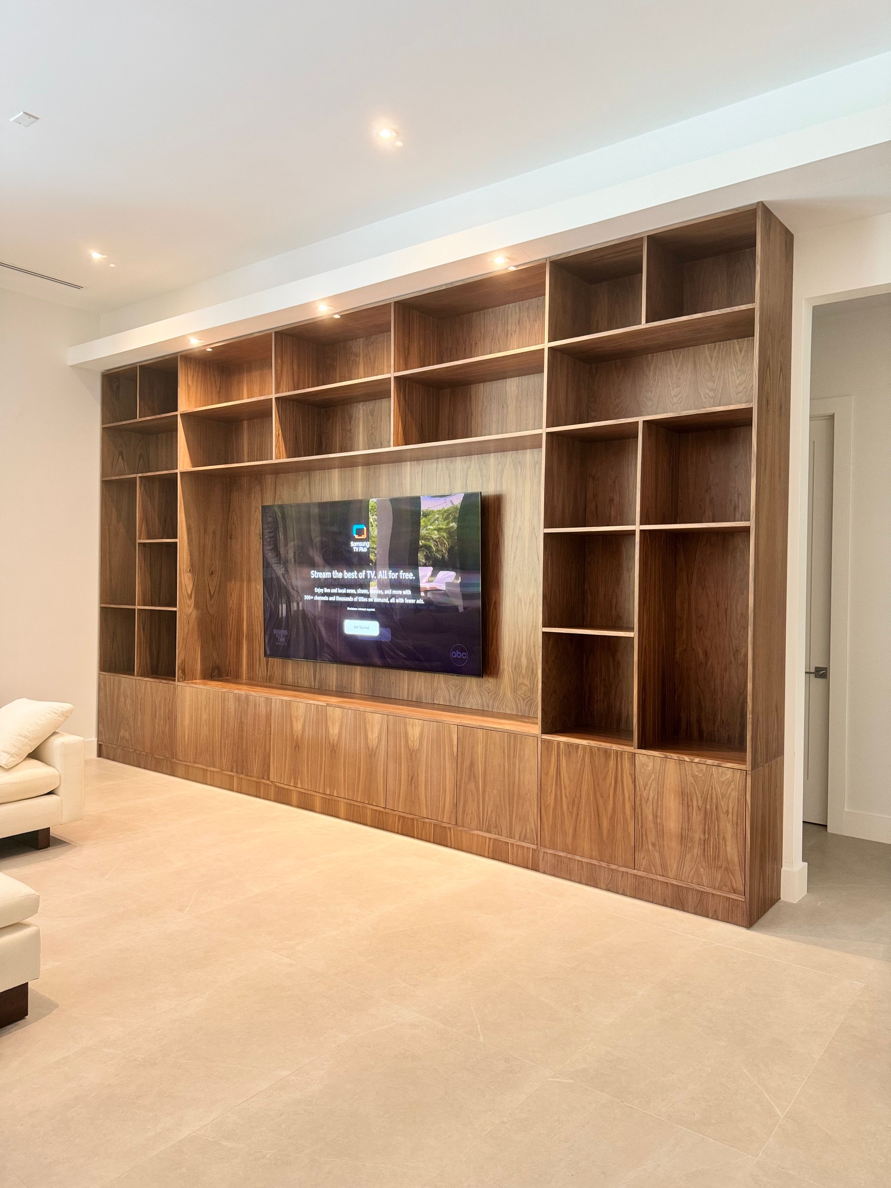 Full-wall walnut veneer entertainment unit with open shelving, LED lighting, and closed base cabinets