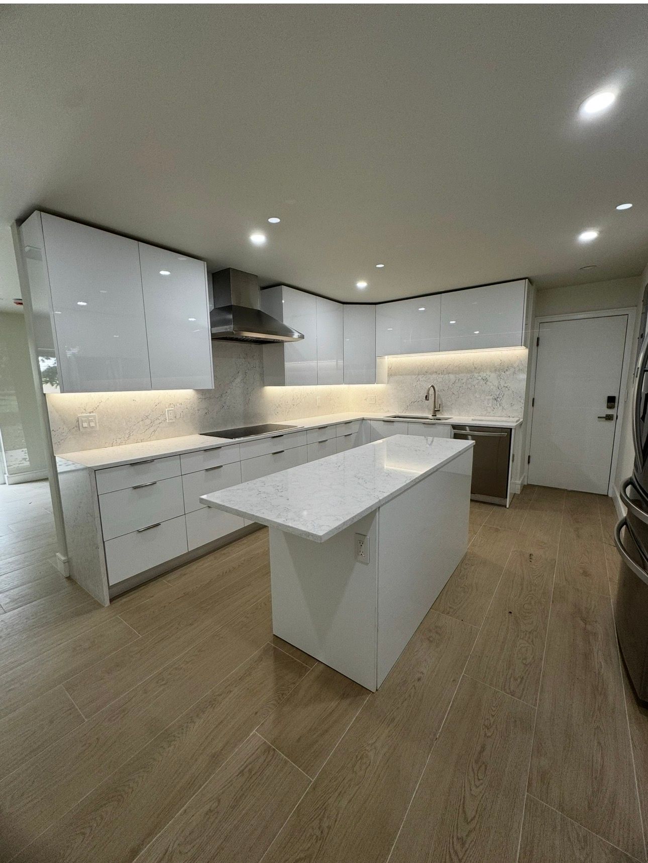 High-gloss white handleless kitchen with quartz island, marble backsplash, and under-cabinet lighting