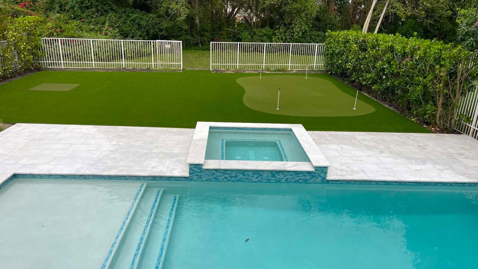 Backyard putting green and artificial lawn beside a pool, installed by Never Ending Green Synthetic Turf
